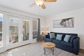 A living room with a dark blue sofa, a wooden coffee table, and a ceiling fan. - Thousand Sunnies (Destin)