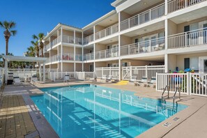 Un hotel de varios pisos con piscina, mobiliario exterior y palmeras.