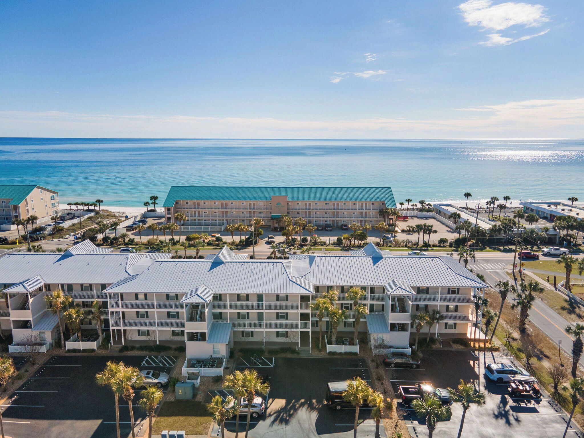 Un hotel sulla spiaggia con diversi edifici, aree parcheggio e vista sull'oceano.