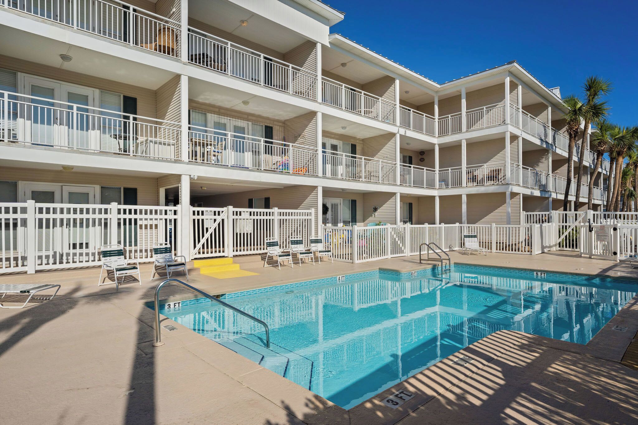 Un hotel de varios pisos con piscina, balcones y palmeras.