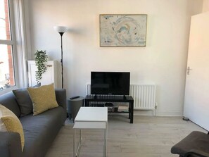 A living room with a sofa, a coffee table, a TV on a stand, a floor lamp, and a painting on the wall. - Spacious 3-Bed Apartment in Queen's Quarter (Belfast)