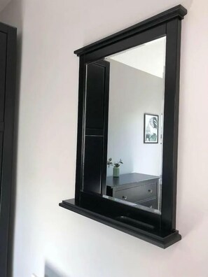 A wall-mounted mirror with a black frame and a shelf below it. - Spacious 3-Bed Apartment in Queen's Quarter (Belfast)