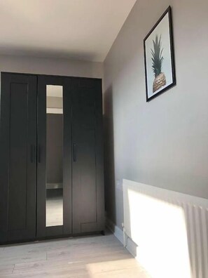 A room with a wardrobe, a framed pineapple picture on the wall, and a radiator. - Spacious 3-Bed Apartment in Queen's Quarter (Belfast)