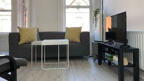 A living room with a sofa, a coffee table, a TV stand, and a radiator. - Spacious 3-Bed Apartment in Queen's Quarter (Belfast)
