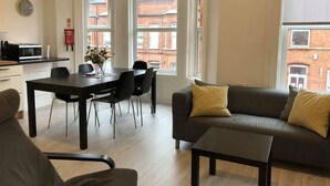 A modern living room with a sofa, a coffee table, and a dining area with chairs and a table. - Spacious 3-Bed Apartment in Queen's Quarter (Belfast)
