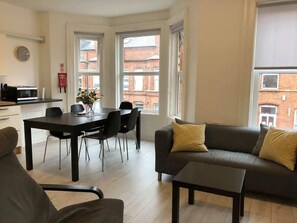 A modern living room with a sofa, a coffee table, and a dining area with chairs and a table. - Spacious 3-Bed Apartment in Queen's Quarter (Belfast)
