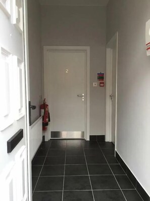 A hallway with a white door marked with the number 2, a fire extinguisher, and a fire alarm on the wall. - Spacious 3-Bed Apartment in Queen's Quarter (Belfast)
