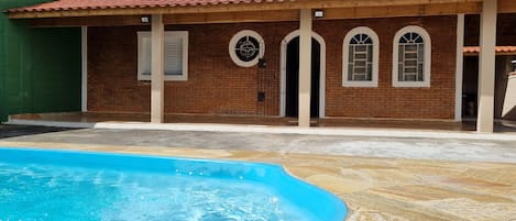 Una casa con piscina, fachada de ladrillo y techo de tejas.