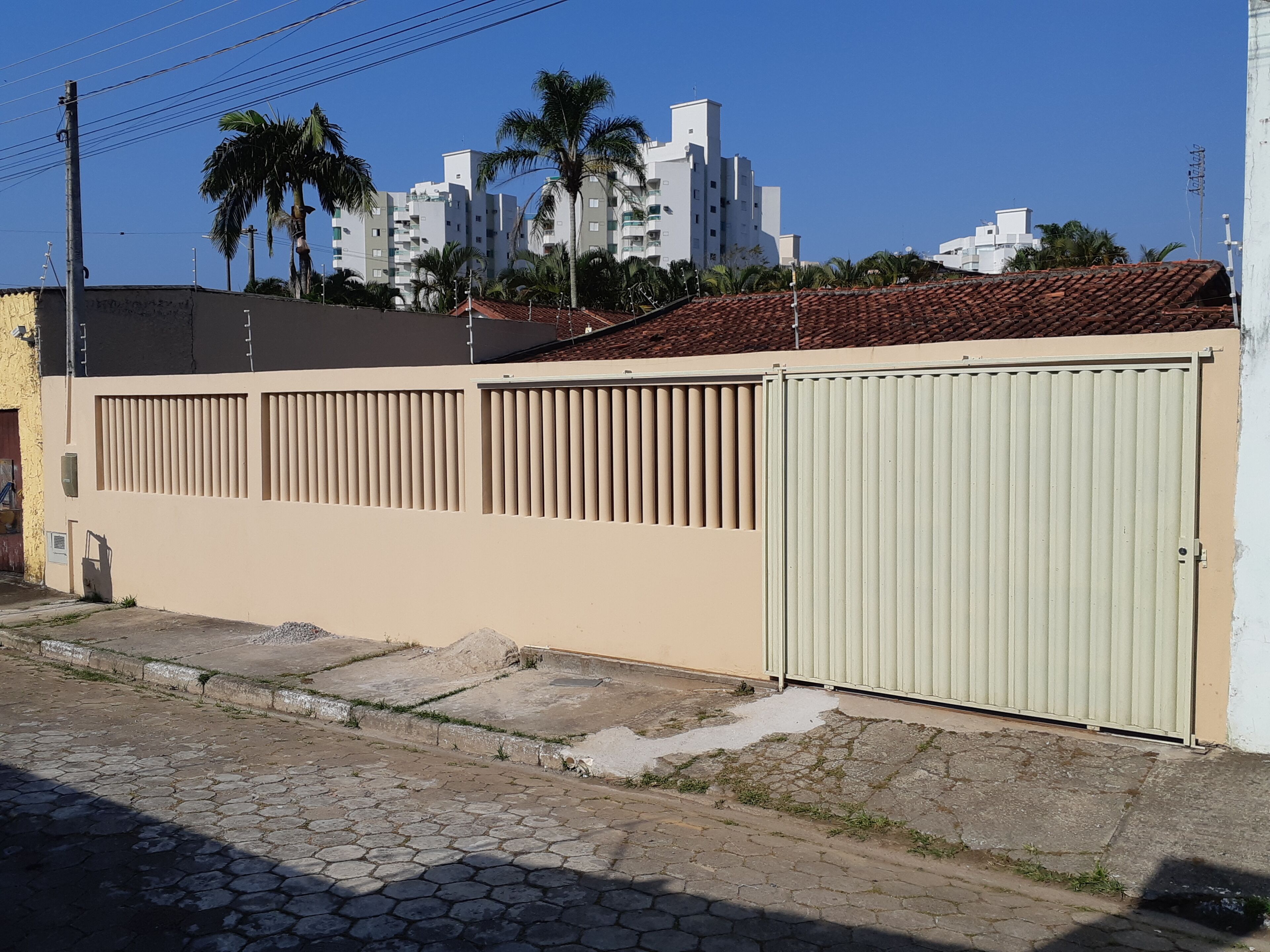 A beige building with a gated entrance, a paved street, and palm trees in the background.
