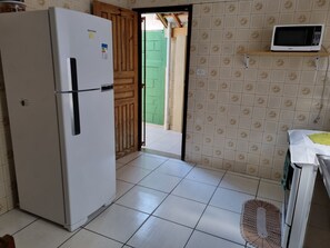 Cocina compacta con un refrigerador blanco, un microondas en un estante y una puerta verde que da al exterior.