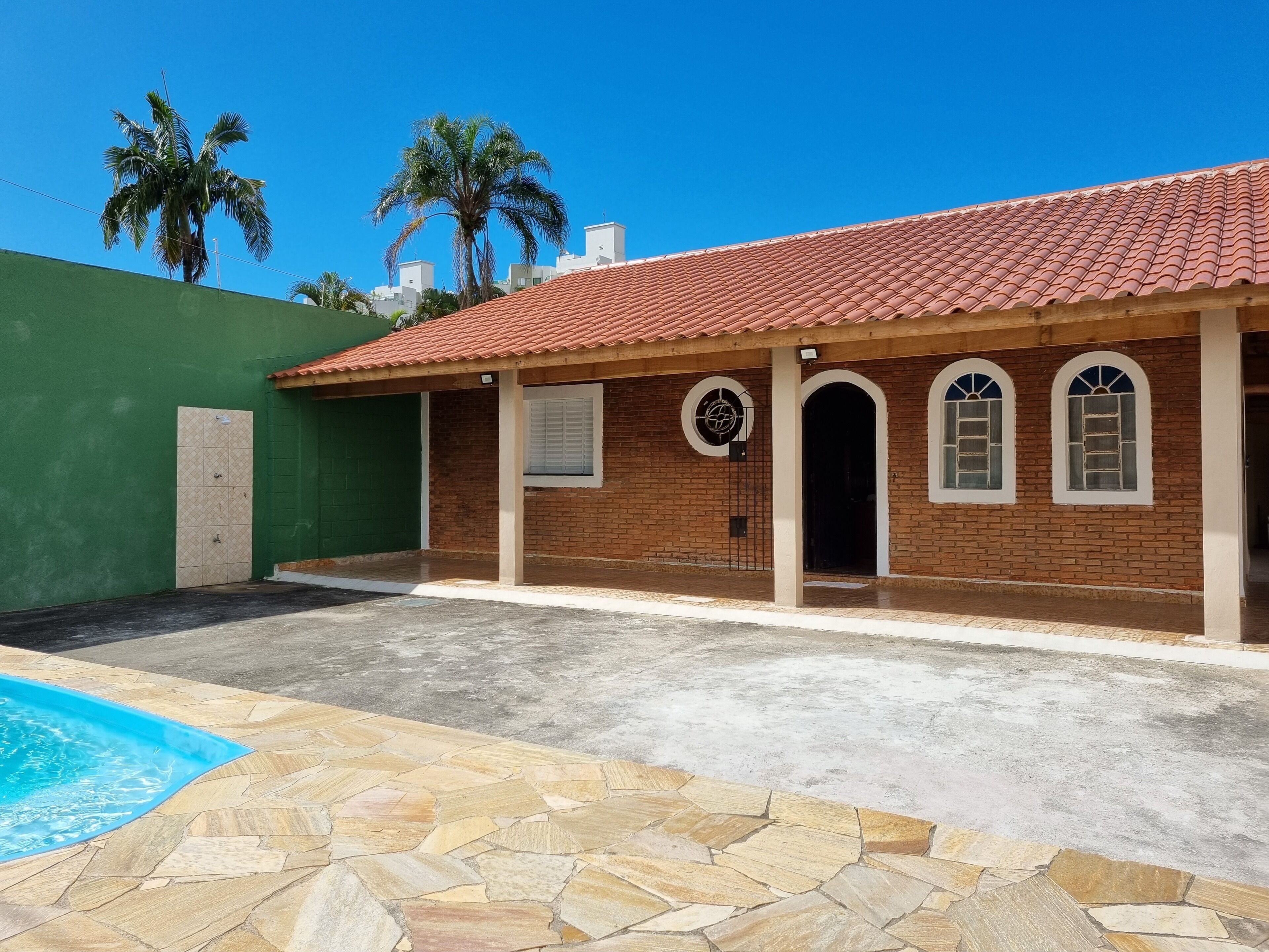 A two-story building with a tiled roof, a swimming pool, and a green wall.