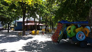 Zona d'estar a l'aire lliure amb cadires i taules grogues, una zona coberta per seure i una exhibició colorida d'anells inflables.