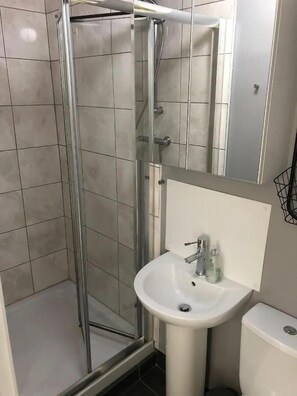 Ein Badezimmer mit Duschkabine aus Glas, einem weißen Waschbecken und einer Toilette.