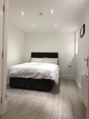 A bedroom with a bed, white walls, and a wooden floor. - Stylish 2 BR Queens Quarter Ground Floor Apartment (Belfast)