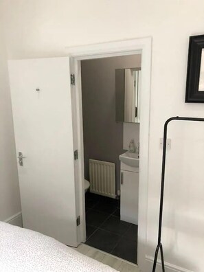 A room with a white door, a white radiator, a white sink, and a mirror above the sink. - Stylish 2 BR Queens Quarter Ground Floor Apartment (Belfast)
