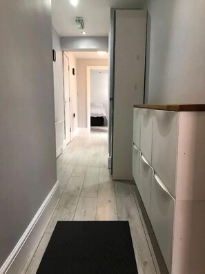 Ein schmaler Flur mit schwarzer Fußmatte am Eingang, der zu einem Schlafzimmer mit Bett und Kleiderschrank führt.