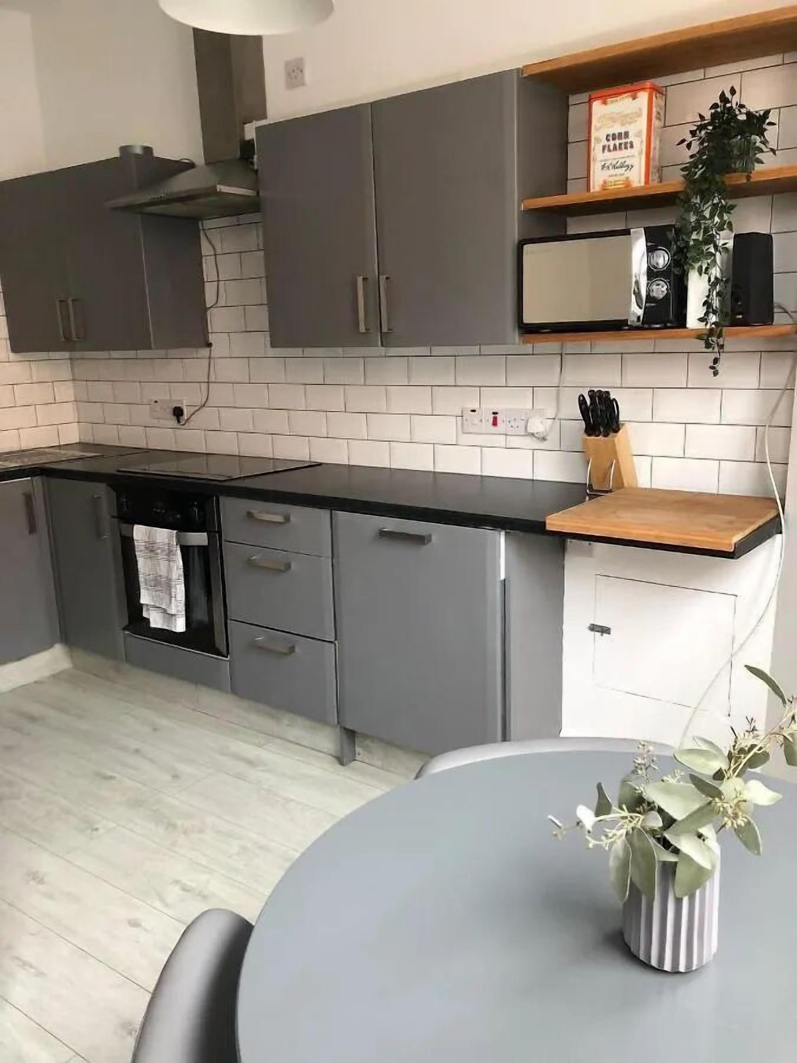 A modern kitchen with grey cabinets, a black countertop, and a wooden table with a vase of flowers.