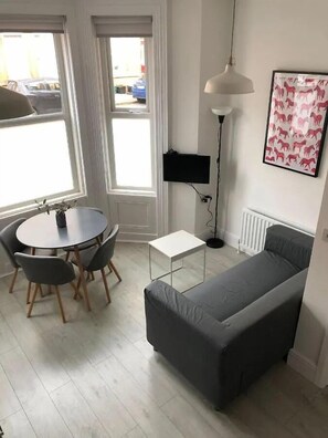 A compact living space with a dining table, a sofa, a floor lamp, and a radiator. - Stylish 2 BR Queens Quarter Ground Floor Apartment (Belfast)