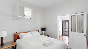 Quarto de hotel com cama, mesas de cabeceira, abajur, espelho e porta que dá para uma varanda.