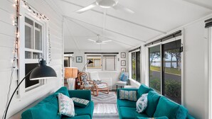 A spacious room with teal sofas, a ceiling fan, and large windows offering a view of the outdoors.