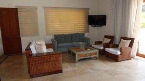 A living room with a sofa, two armchairs, a coffee table, a television, and a door. - Caribbean Bungallow With 2 Bedrooms in Cap Cana (Punta Cana)