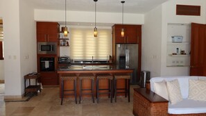 A modern kitchen with a central island, bar stools, a refrigerator, and a microwave. - Caribbean Bungallow With 2 Bedrooms in Cap Cana (Punta Cana)