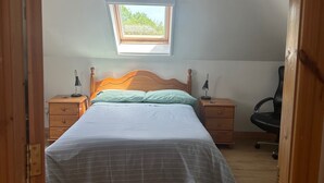 Ein Schlafzimmer mit einem Bett, einem Nachttisch, einem Schreibtisch, einem Sessel, einem Fenster und einer Pendelleuchte.