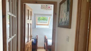 Ein schmaler Flur führt zu einem Schlafzimmer mit Dachfenster, Holzdielen und einem Gemälde an der Wand.