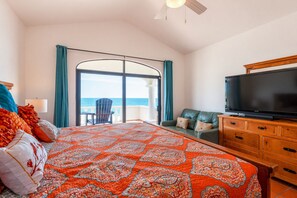 Ein Schlafzimmer mit einem großen Bett, einem Fernseher, einer Couch und Blick auf den Ozean durch ein großes Fenster.