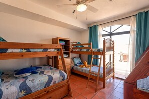 Ein Zimmer mit Etagenbetten, einer Holzleiter, einer Regalwand und einem Fenster mit Vorhängen.
