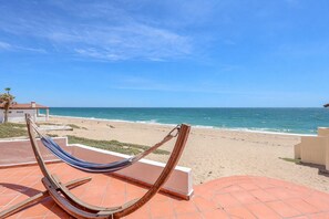 Eine Hängematte auf einer gefliesten Terrasse mit Blick auf einen Strand unter blauem Himmel.
