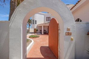 Ein gebogener Eingang zu einem Anwesen mit einer gefliesten Terrasse und einem weißen Gebäude im Hintergrund.