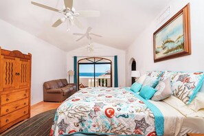 A bedroom with a bed, a wooden wardrobe, a brown leather sofa, a ceiling fan, and a view of the sea through a glass door. - Hacienda Almas Gemelas – Where Luxury Meets the Sea of Cortez (Puerto Peñasco)