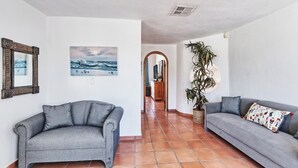 A living room with two grey sofas, a large potted plant, and a painting on the wall. - Hacienda Almas Gemelas – Where Luxury Meets the Sea of Cortez (Puerto Peñasco)
