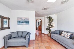 A living room with two grey sofas, a large potted plant, and a painting on the wall. - Hacienda Almas Gemelas – Where Luxury Meets the Sea of Cortez (Puerto Peñasco)