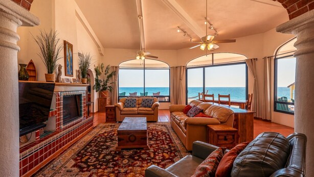 A spacious living room with a fireplace, leather sofas, a coffee table, and a large window overlooking the sea. - Hacienda Almas Gemelas – Where Luxury Meets the Sea of Cortez (Puerto Peñasco)