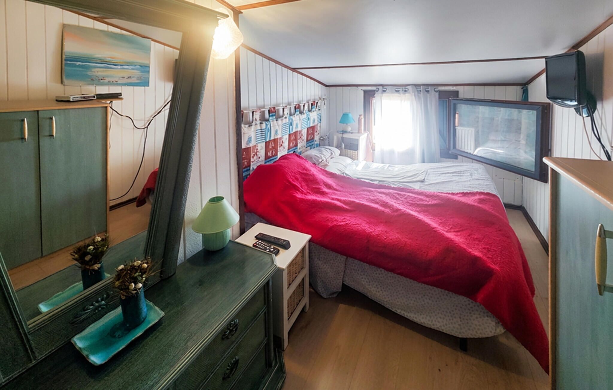 A compact bedroom with a bed, a dresser, a mirror, a lamp, and a television.