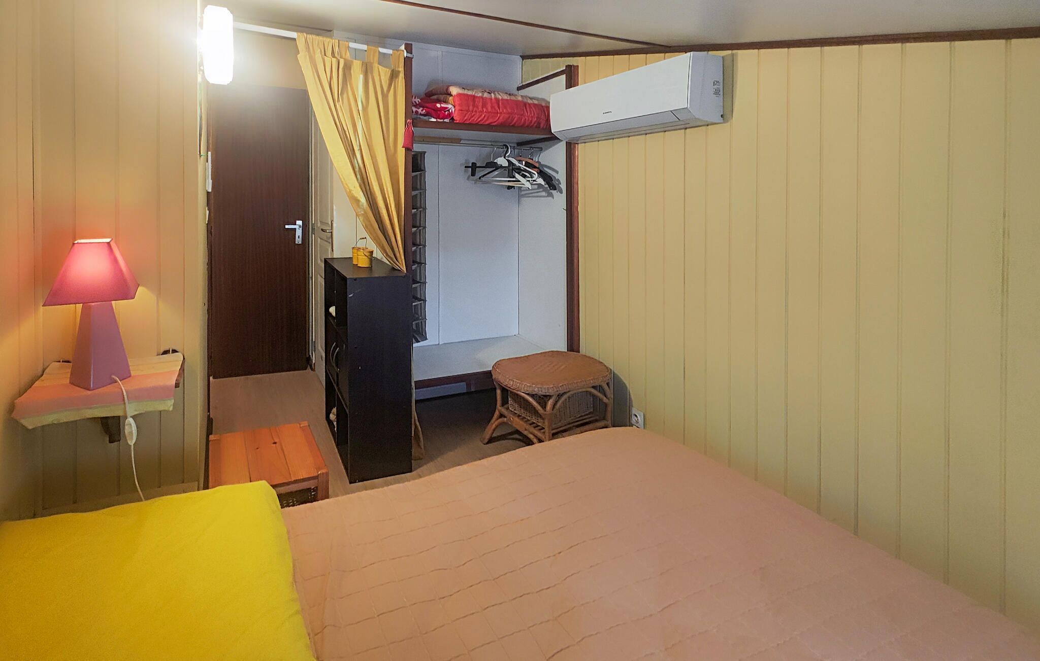 A compact room with a bed, a small stool, a hanging clothes rack, and a wall-mounted air conditioner.