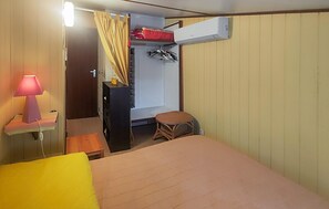 A compact room with a bed, a small stool, a hanging clothes rack, and a wall-mounted air conditioner. - MAISON À 500M DE LA PLAGE (Portiragnes)