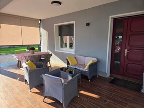 An outdoor patio area with a table and chairs, a sofa, and a red door.