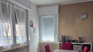 A dining area with a table set for four, a kitchen area with appliances, and a window with curtains.