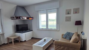 A modern living room with a sofa, a coffee table, a television, and a kitchen area with a window.