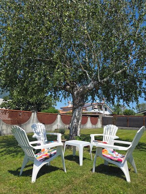 Een terras met witte plastic stoelen en een tafel, omringd door een boom en een hek.