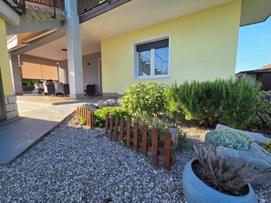 Ein überdachter Außenbereich mit Terrasse, Sitzgelegenheiten und Blick auf ein Gebäude.