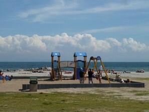 A beach with a playground, including swings and a slide, and a sandy area with people. - The Casa delle Magnolie (Terranova)