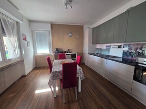 A compact kitchen with modern appliances, a dining area with a table and chairs, and a visible clock on the wall.