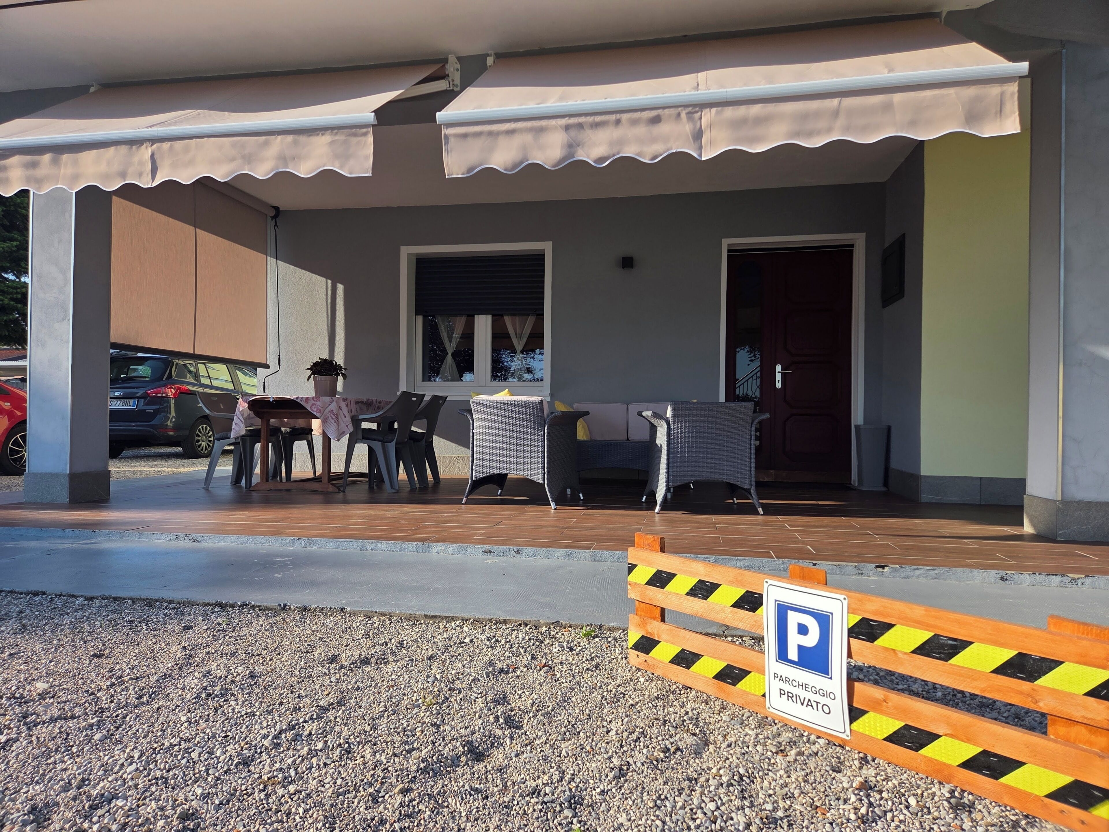 A covered outdoor seating area with tables and chairs, a potted plant, and a vehicle parked outside.