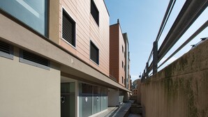 Eine schmale Stadtstraße mit modernen Gebäuden, einem Fußweg und einer sichtbaren Brückenkonstruktion.