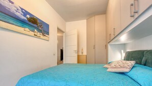 Ein Schlafzimmer mit Bett, Kleiderschrank, einem Bild mit Strandmotiv und einer Tür zu einem anderen Raum.
