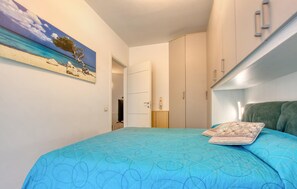 Ein Schlafzimmer mit Bett, Kleiderschrank, einem Bild mit Strandmotiv und einer Tür zu einem anderen Raum.